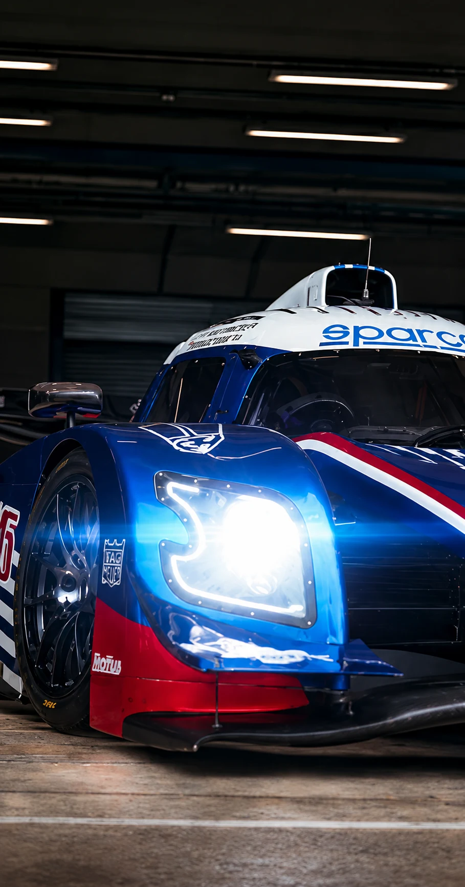 Protótipo de endurance azul, vermelho e branco no box, farol aceso